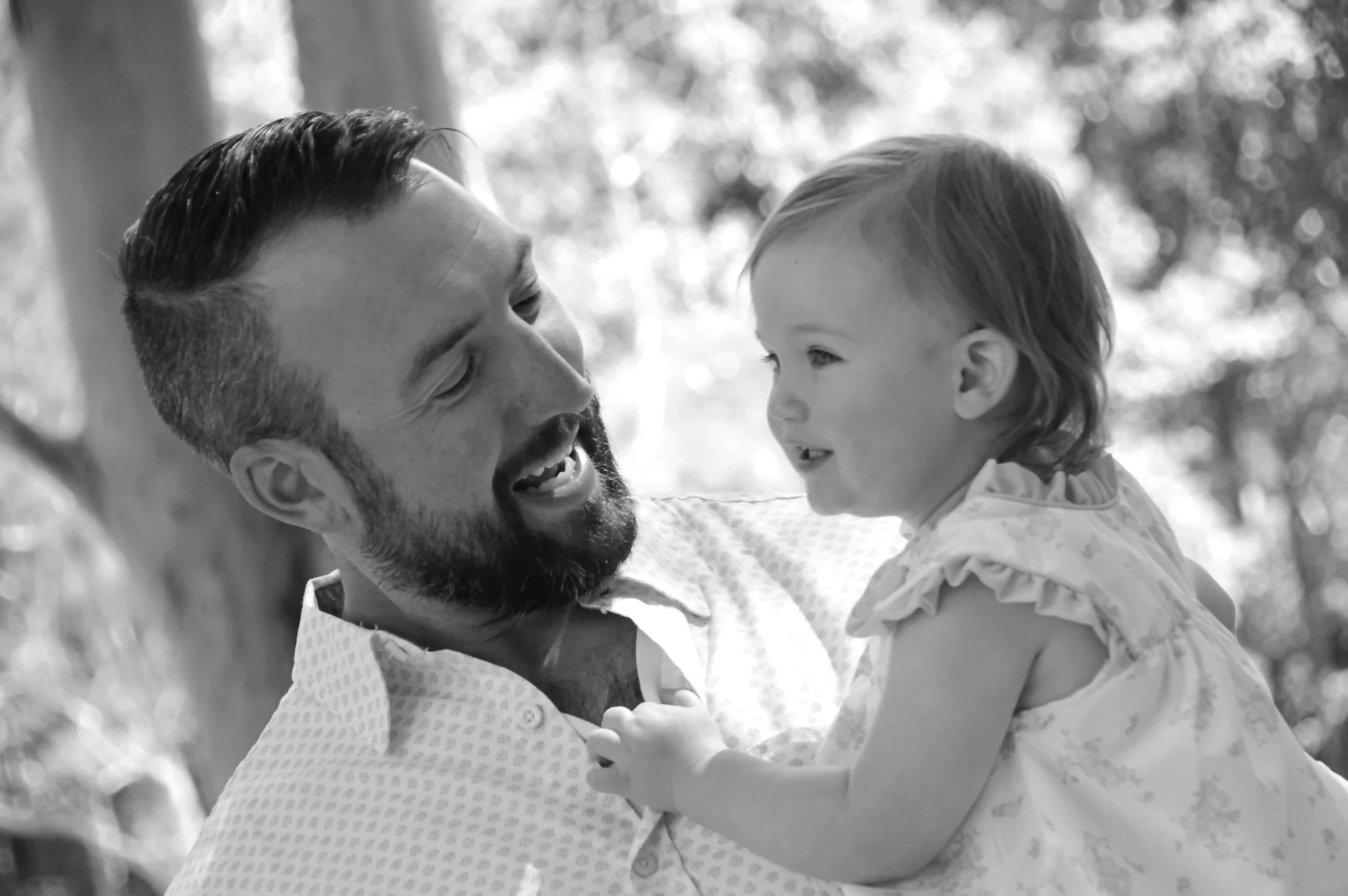 Father smiles warmly at baby held close in black and white.