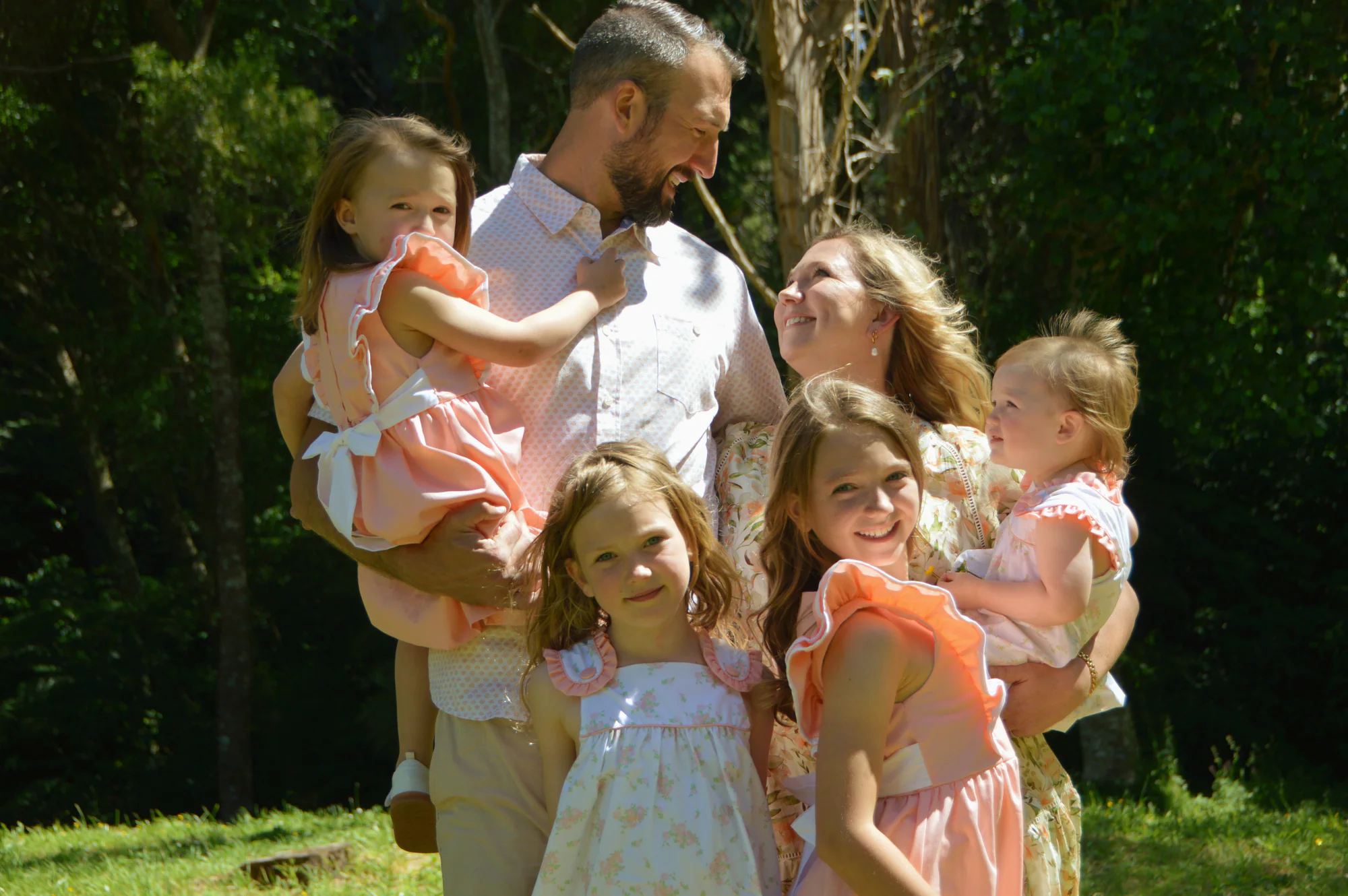 Parents and four daughters share a relaxed moment in bright woodland.