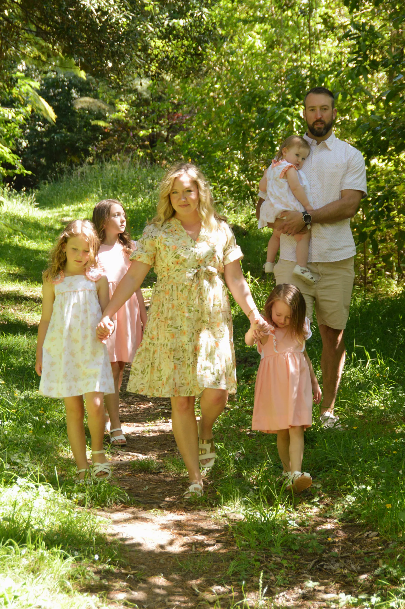 Family of six walks hand in hand along a woodland path.