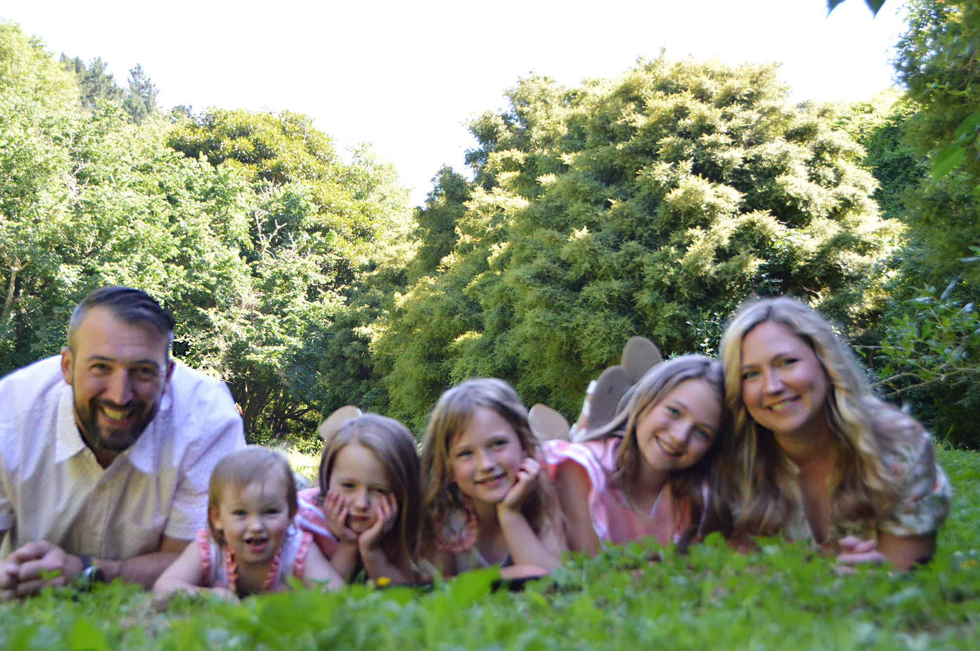 Parents and four daughters lie smiling together on green grass.