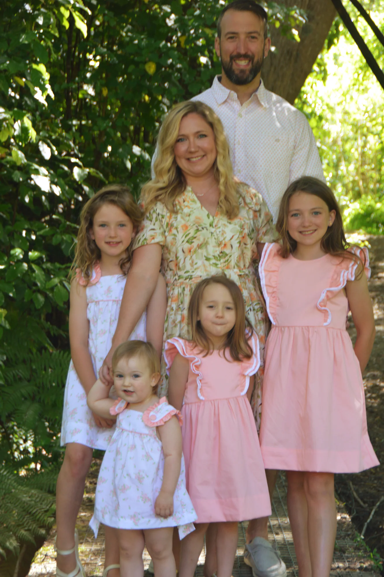 Parents and four daughters stand together on a shaded path.