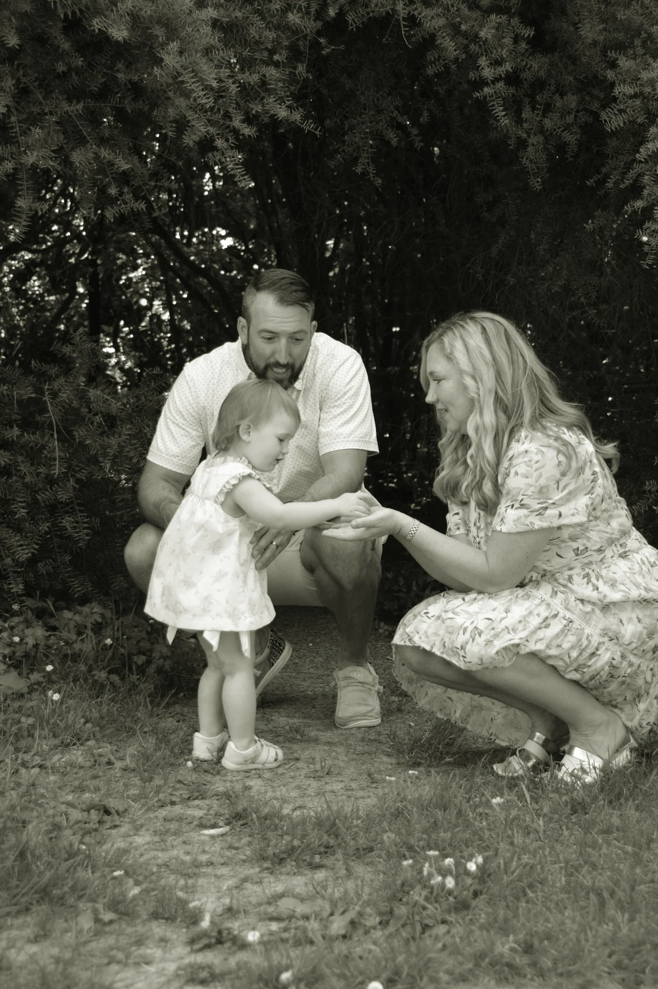 Parents encourage toddler taking steps on a woodland path.