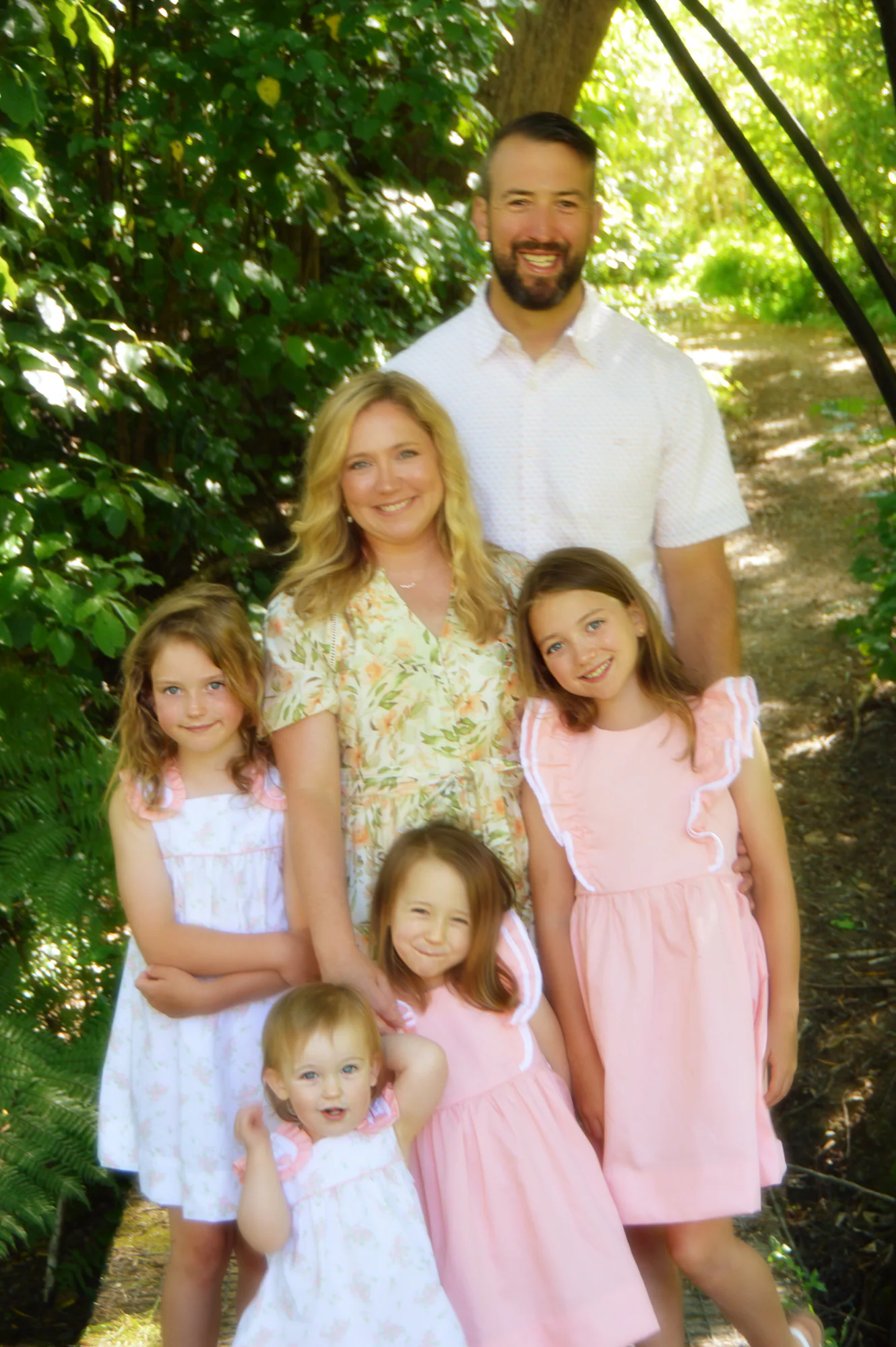 Parents and four daughters pose together beneath arching branches.