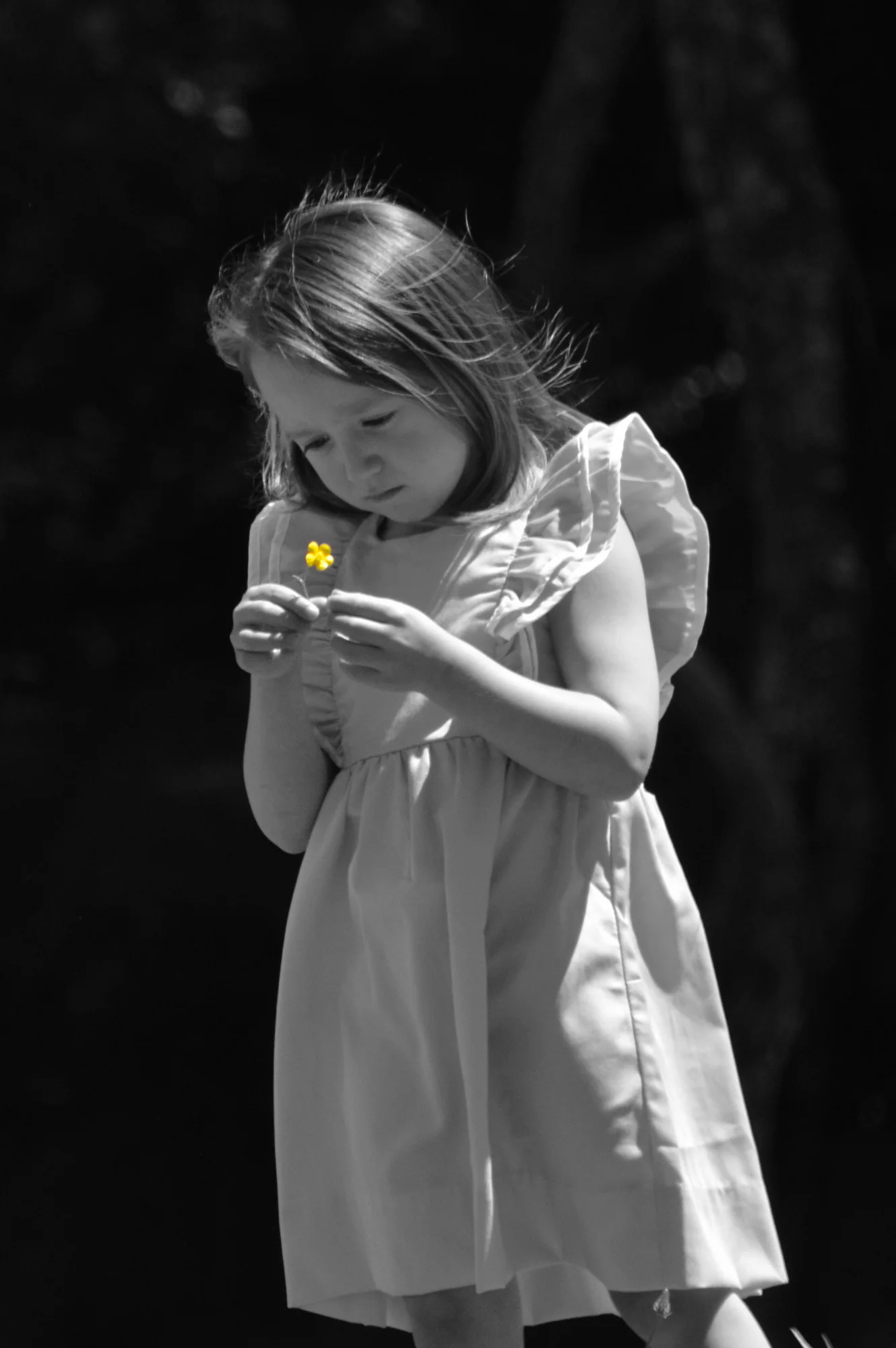 Girl studies a yellow flower against a black and white background.