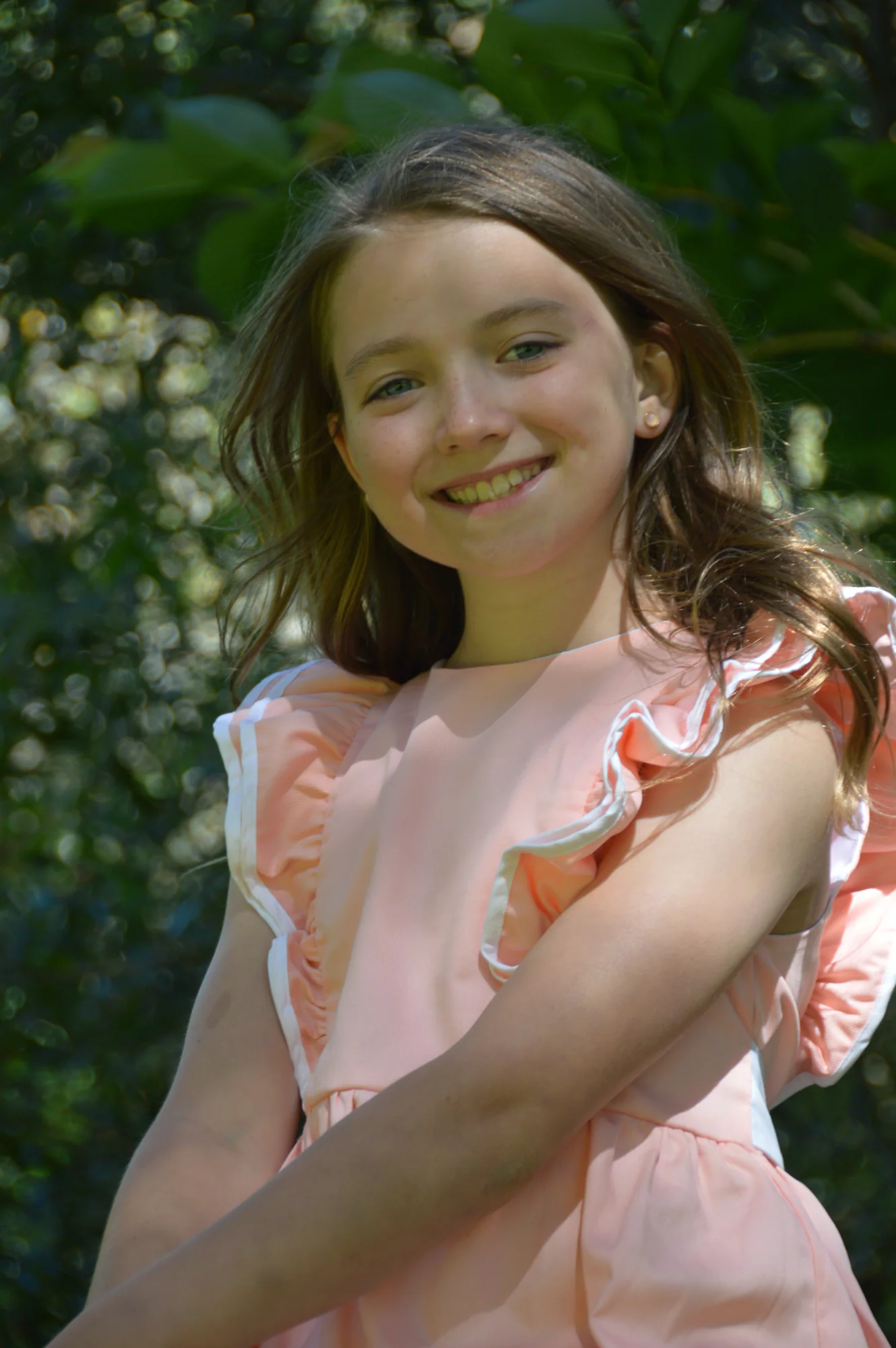 Smiling girl in pink dress poses against dark green foliage.