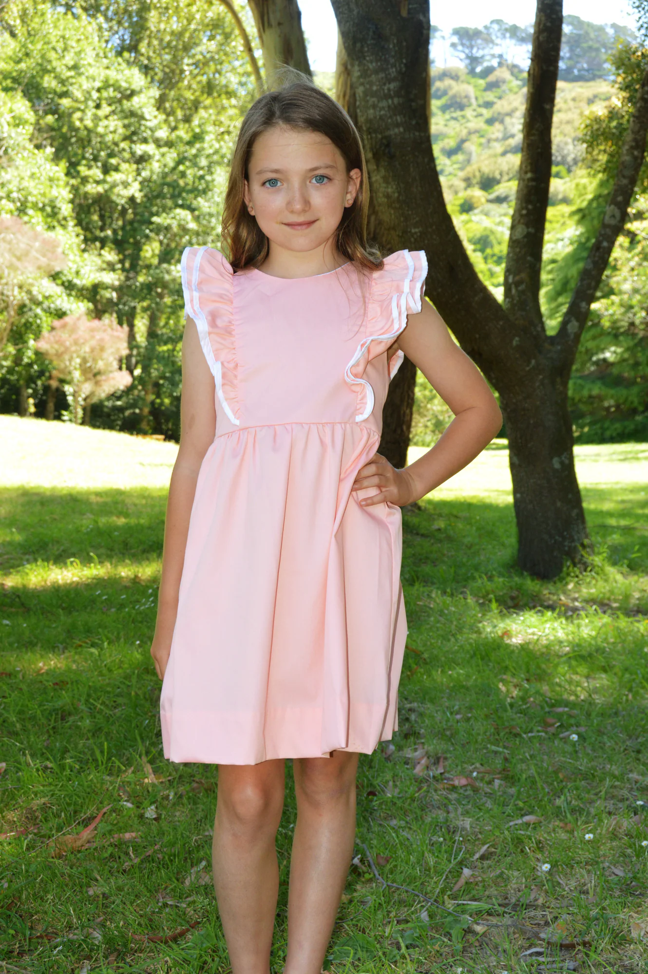 Young girl in pink dress stands beneath trees in a garden.