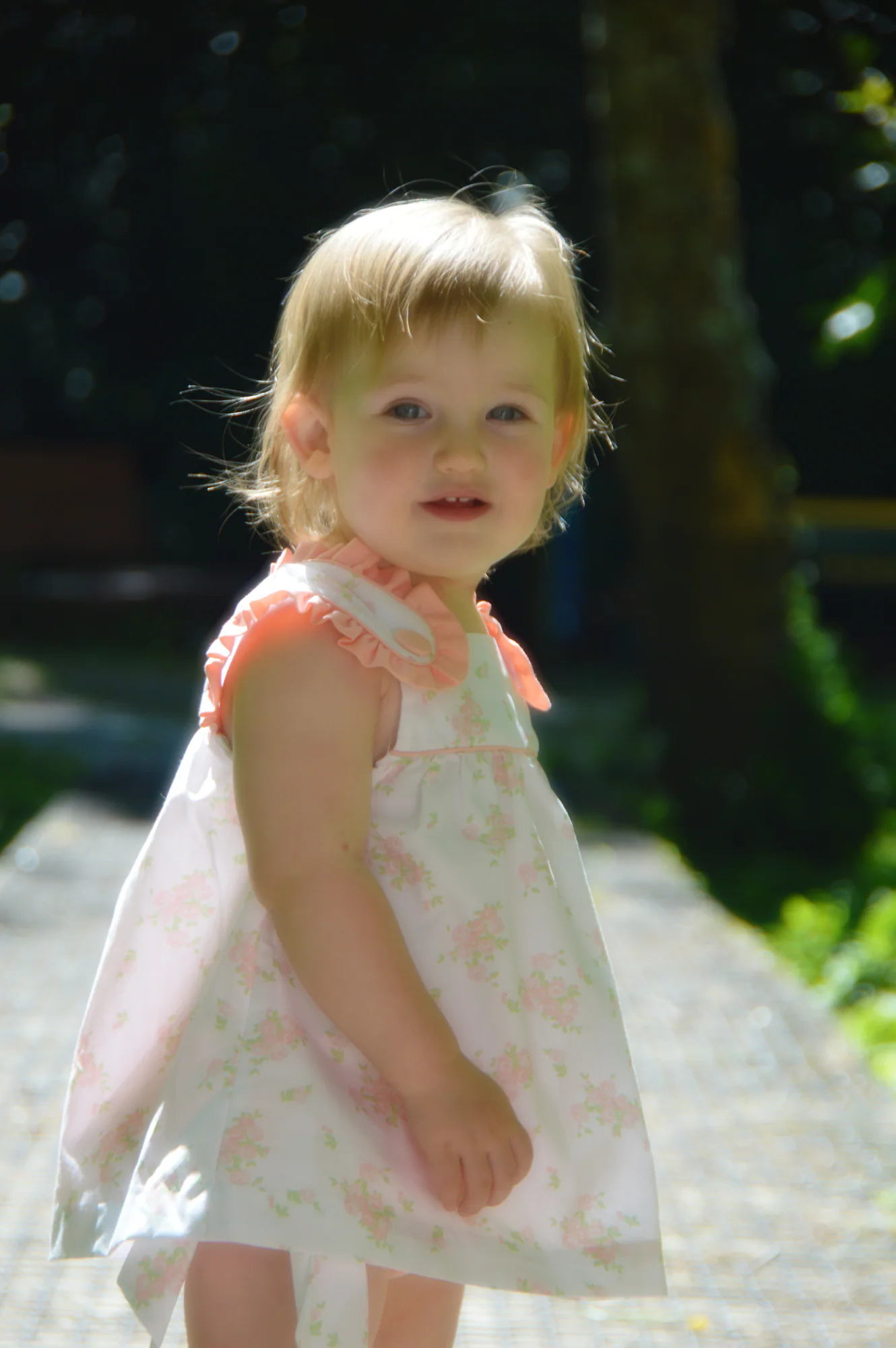 Toddler in floral dress looks toward camera on garden path.