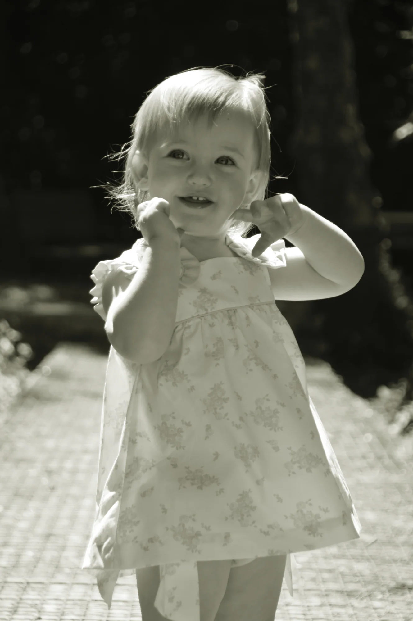Toddler touches her ear while standing on a garden path.