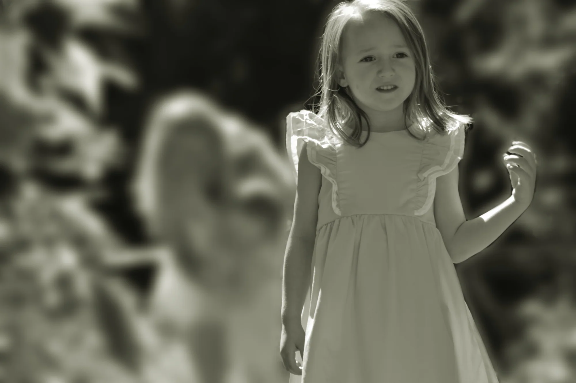 Young girl stands before blurred adult in soft black and white.