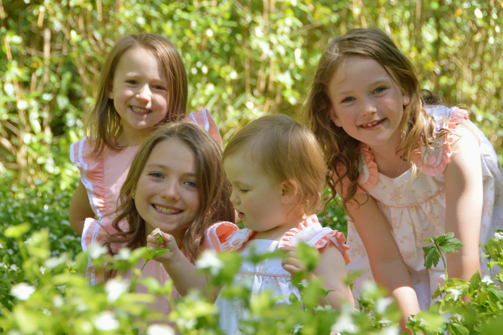 Four sisters smile together among white flowers and green foliage.