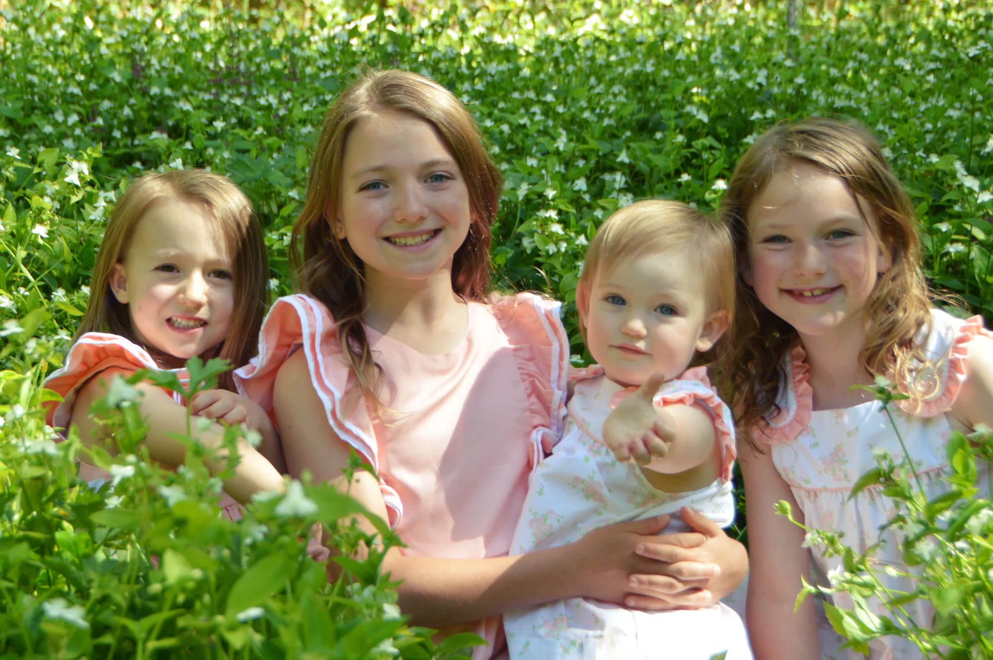 Four sisters pose closely together in a field of white flowers.