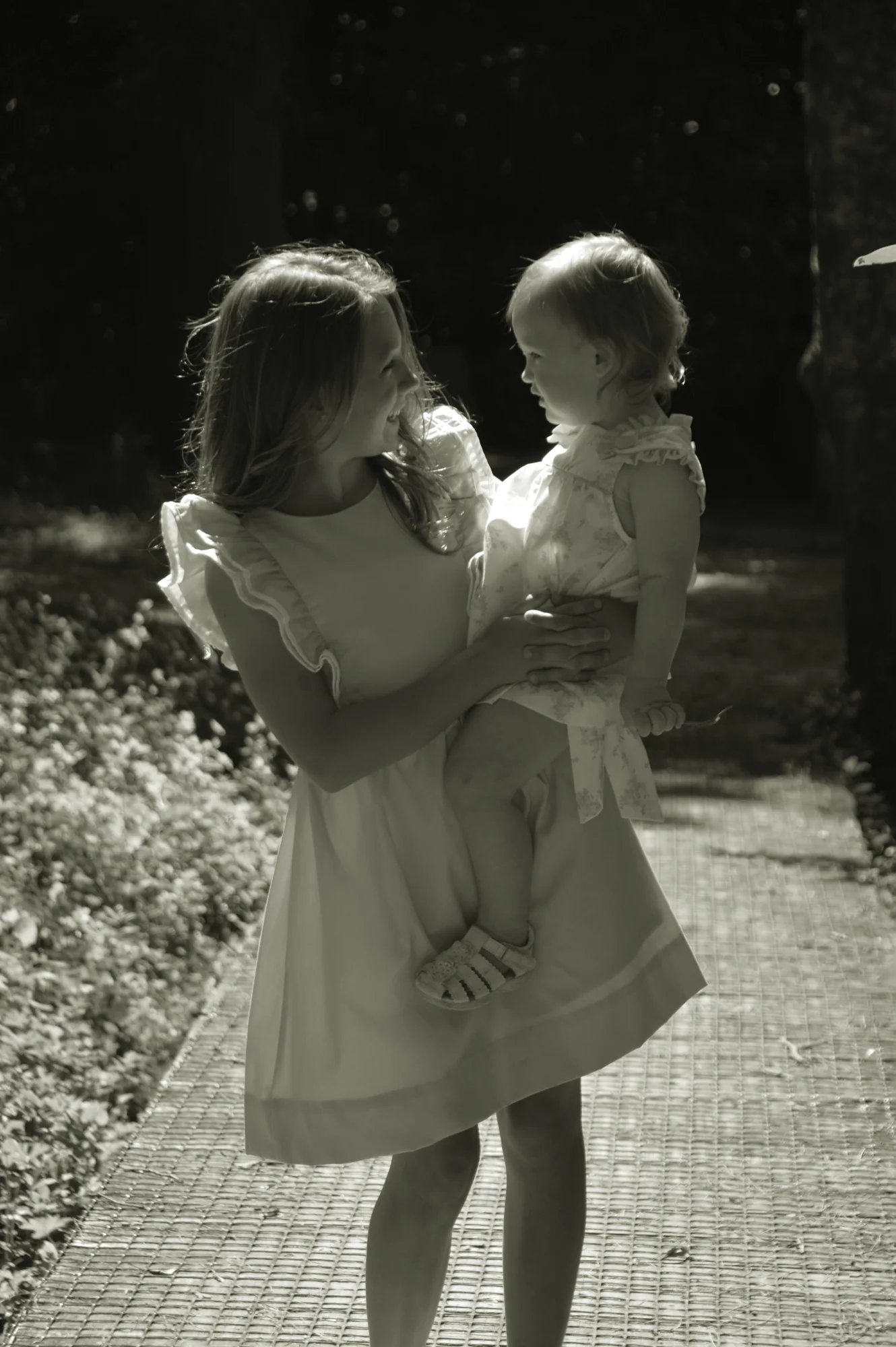 Older sister holds baby face to face in black and white.