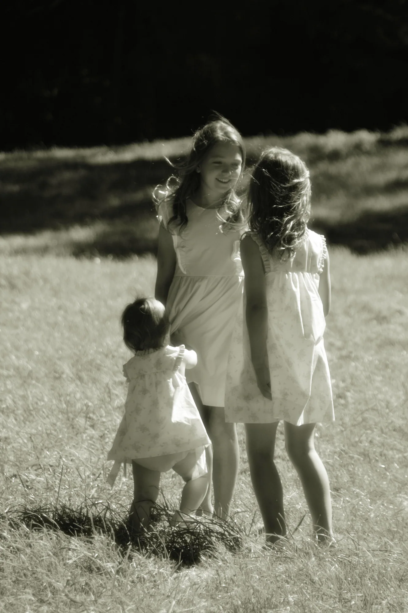 Three sisters gather in a grassy field in black and white.