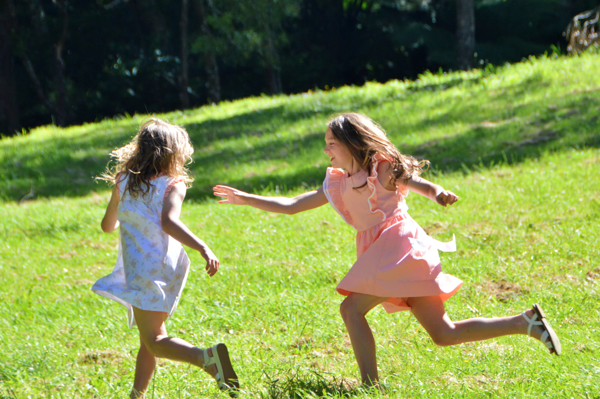 Two girls run toward each other laughing across sunlit grass.