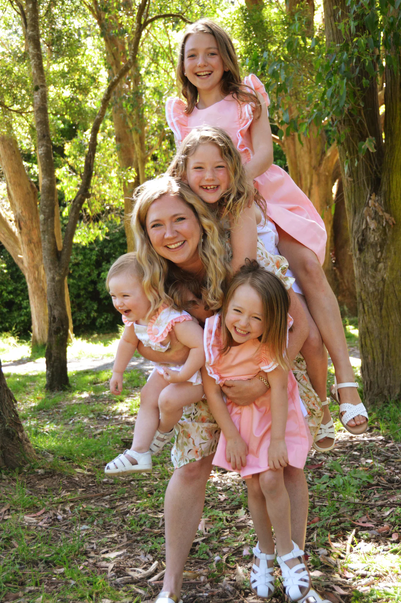 Laughing mother carries four daughters in a playful family stack.