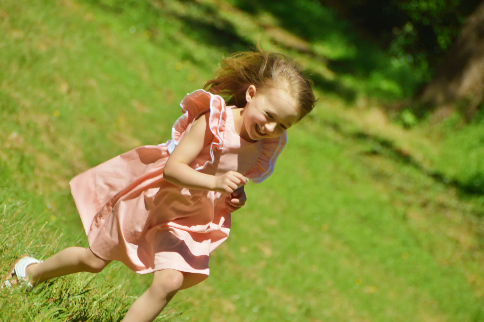 Laughing girl runs across grass in a flowing pink dress.