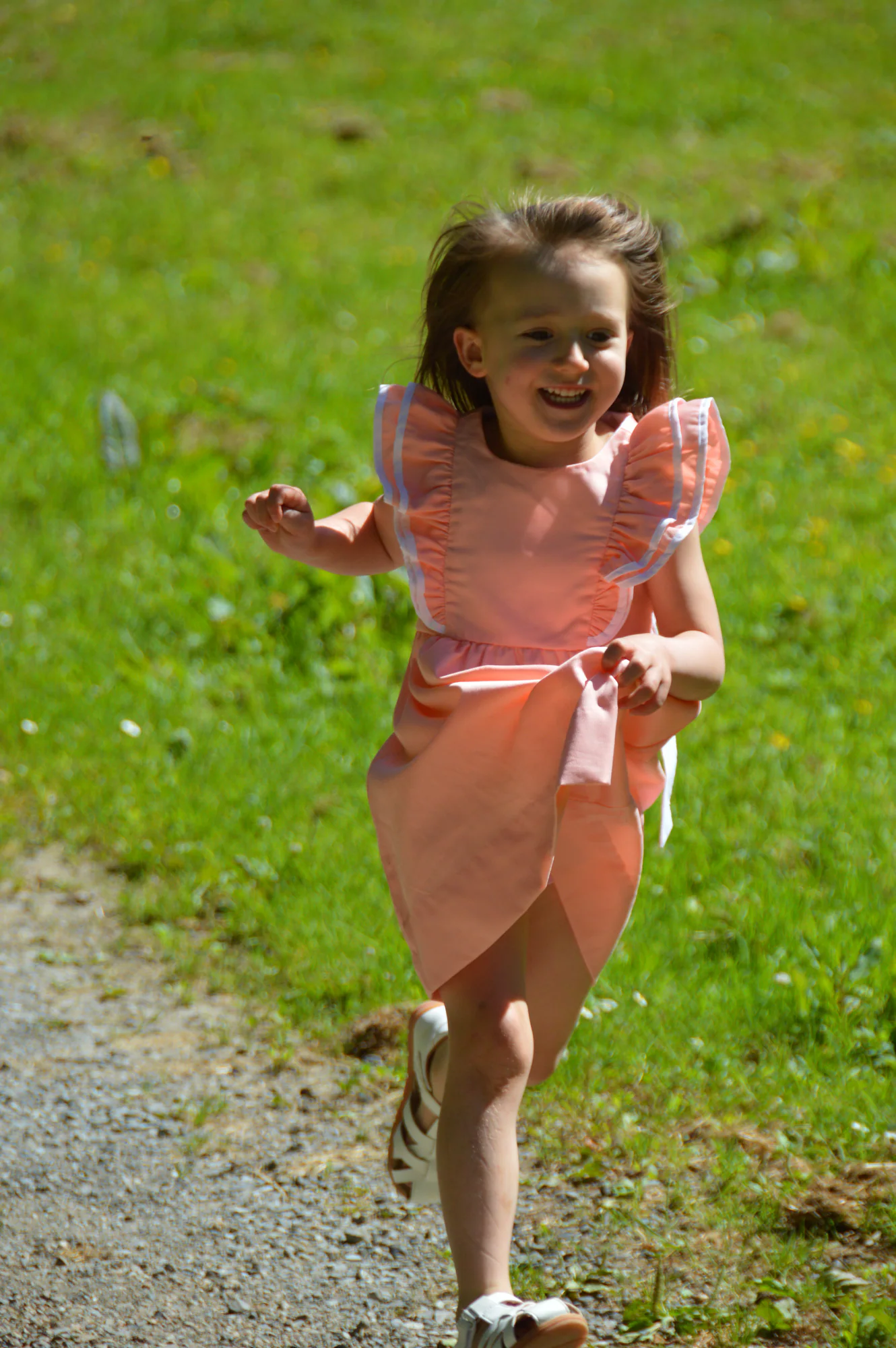 Young girl runs laughing along a sunlit gravel path.