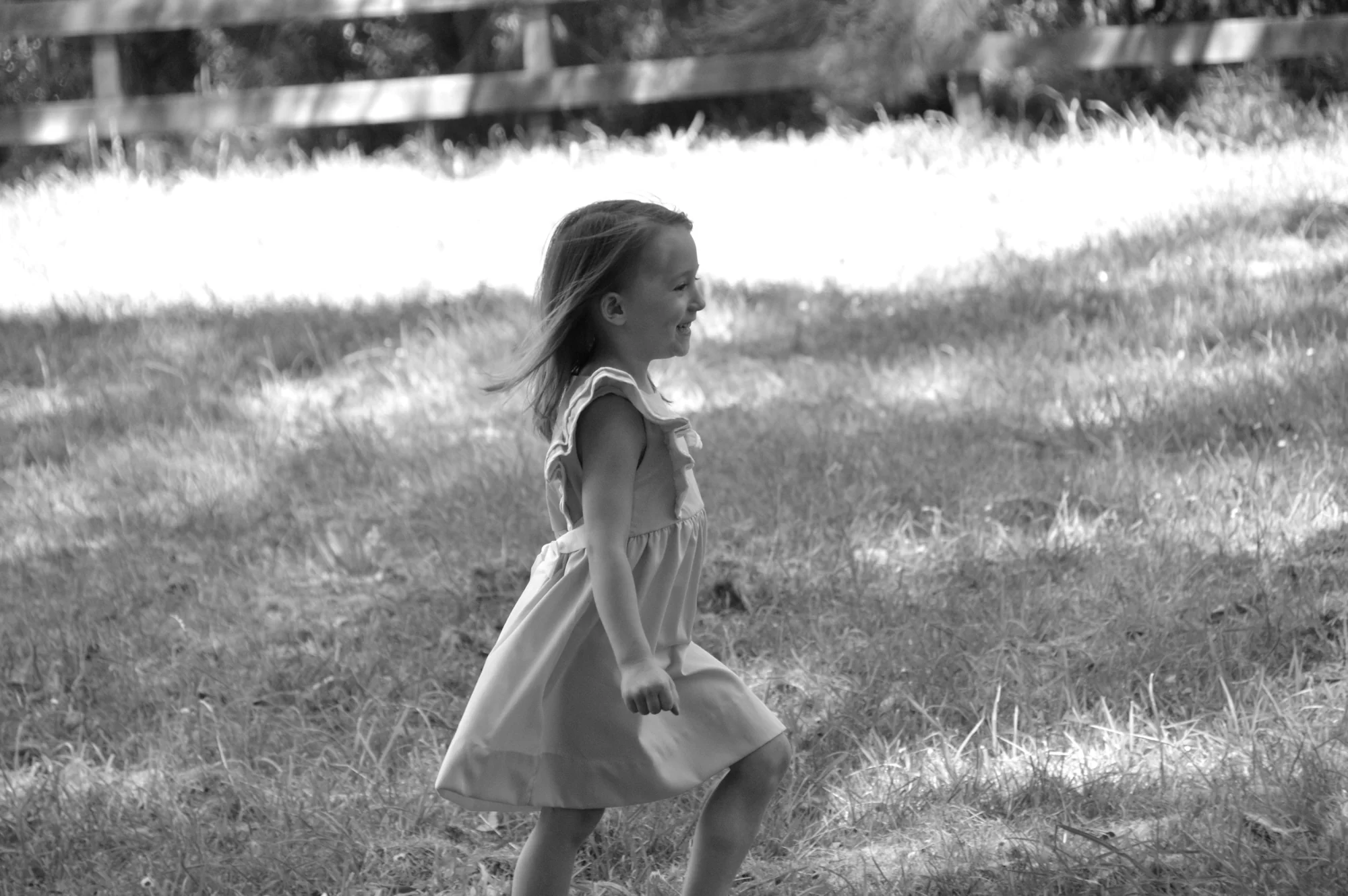 Girl in flowing dress walks through grass in black and white.