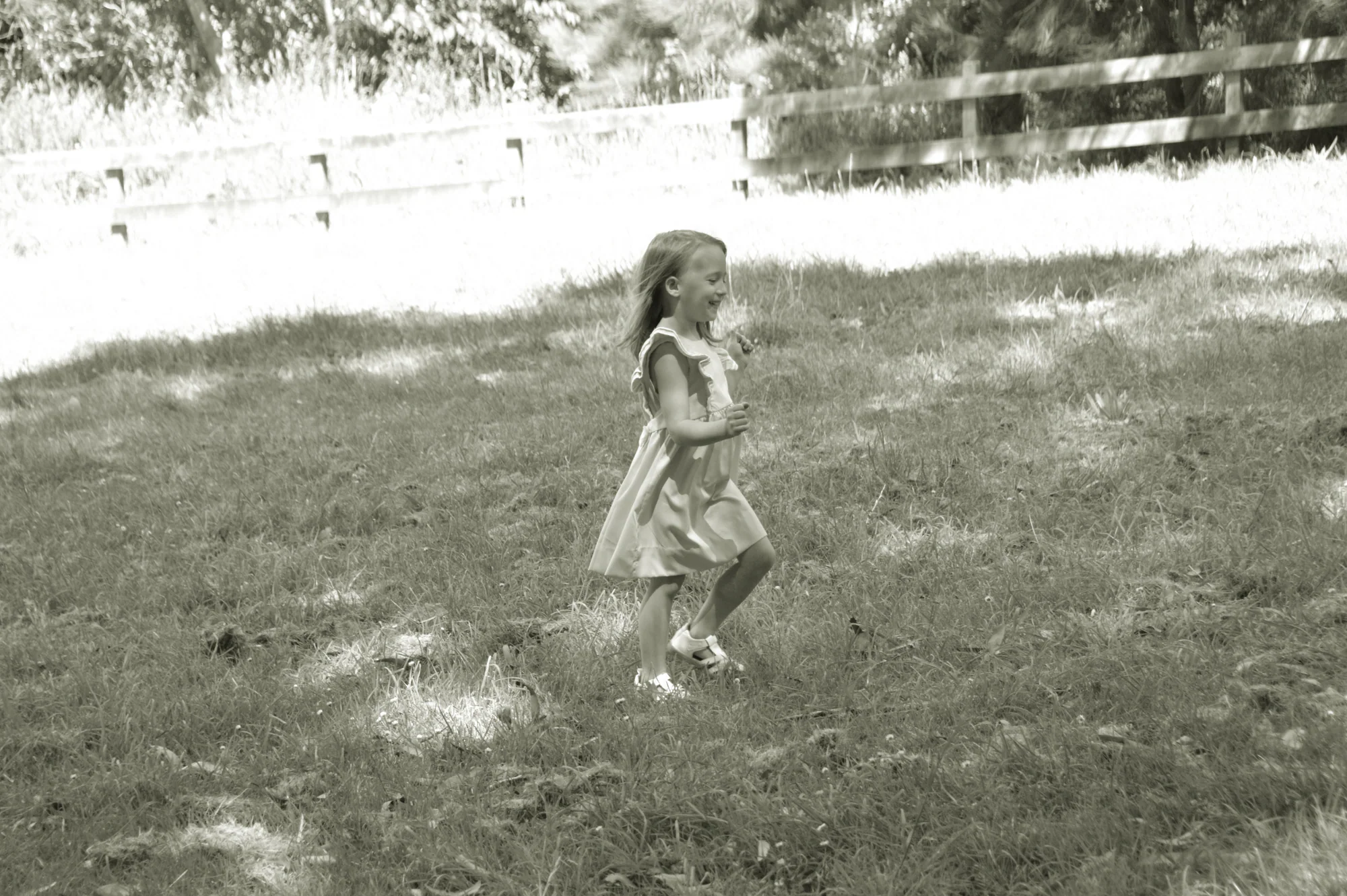 Young girl walks across sunlit grass in soft black and white.